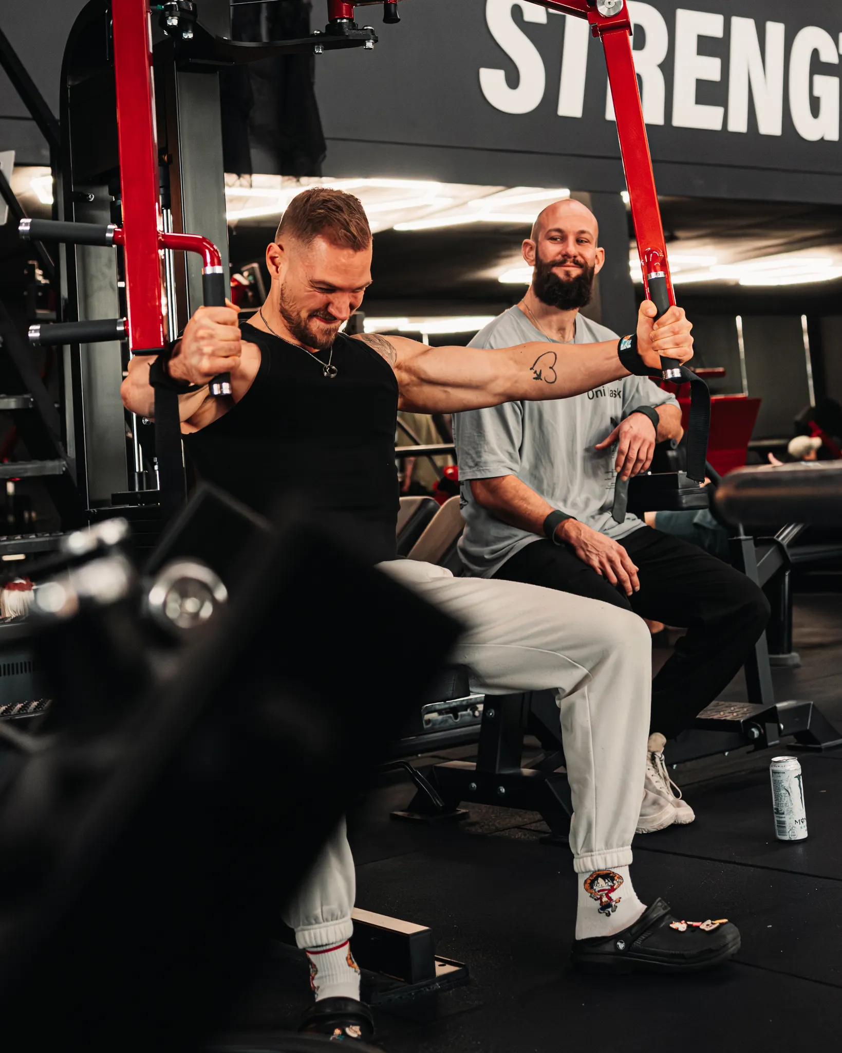 Een coach zit naast een lid op de chest press en kijkt mee terwijl hij de beweging maakt