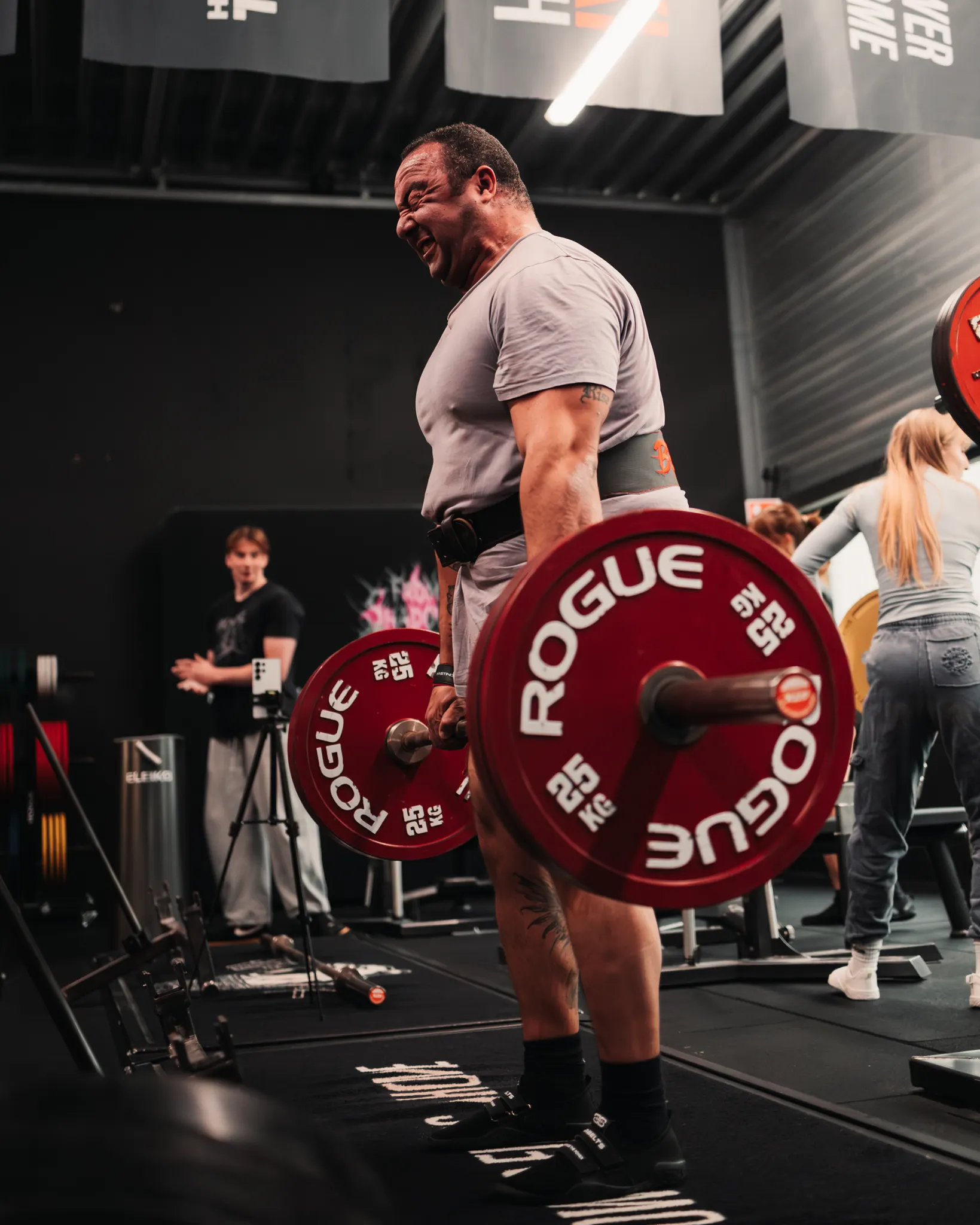 Lifter trekt een zware deadlift met rode Rogue-wedstrijdschijven terwijl anderen toekijken